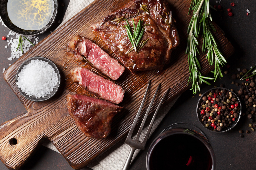 Medium rare steak on a wooden chopping board garnished with rosemary