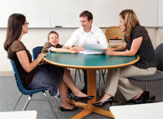 three adults sitting around a table looking at a child